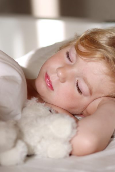 Sweet little child sleeping in bed. Healthy kid, blonde toddler girl, resting in bed in white sunny bedroom.